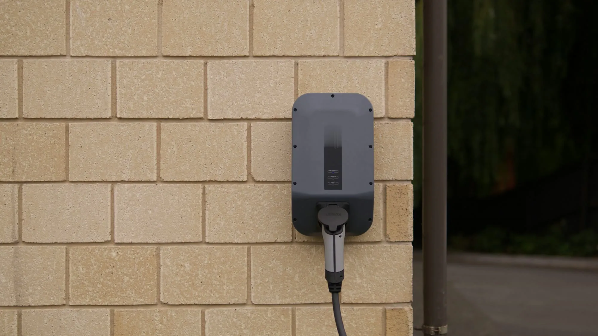 Wallbox ohne Markenlogo an der Wand eines Holzcarports, Ladekabel ordentlich aufgerollt