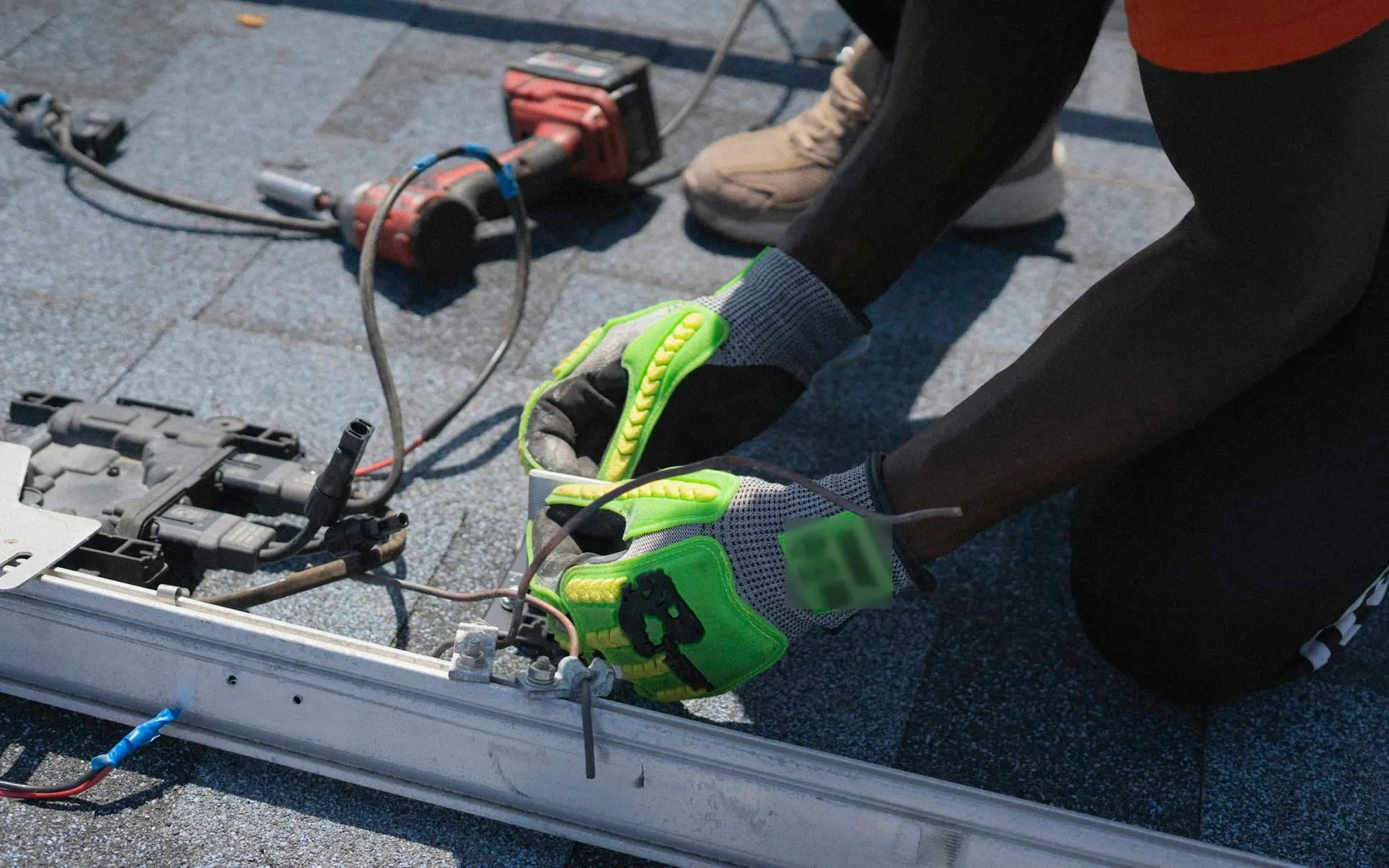 Handwerker von hinten beim Befestigen einer Montageschiene auf Dachziegeln, ohne erkennbares Gesicht