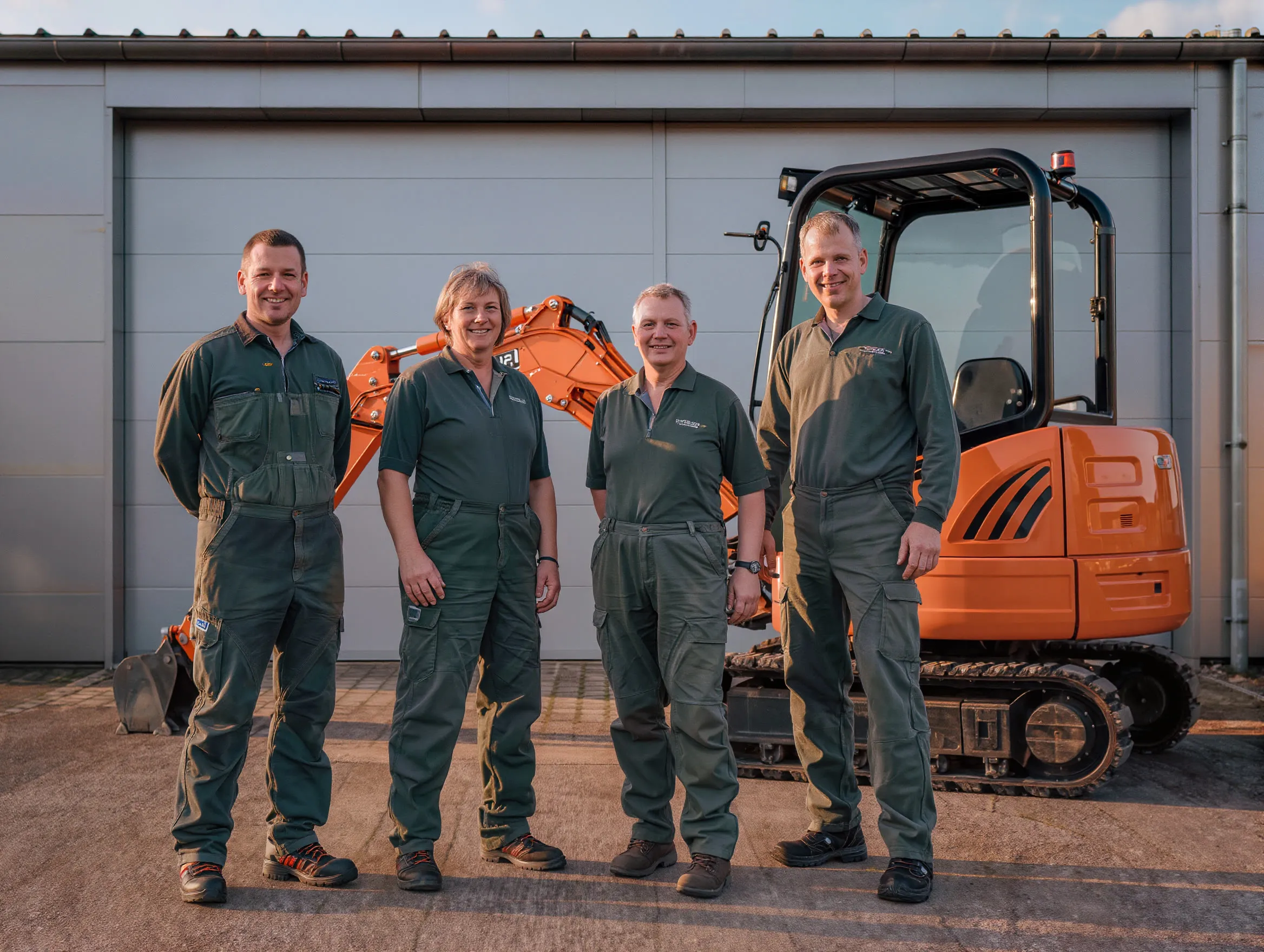 Team eines Gartenbaubetriebs in Arbeitskleidung vor einer Halle mit Minibagger