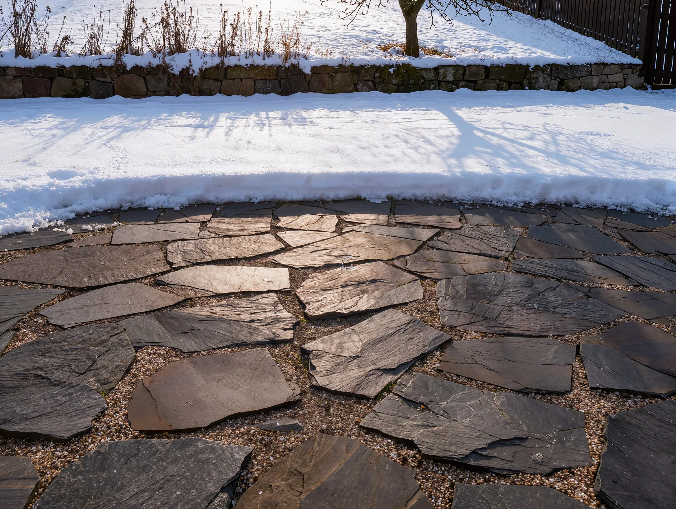 Garten im Winter: Schnee auf Rasen und Beeten, die Natursteinterrasse geräumt